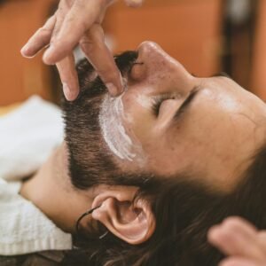 A man with long hair receives a beard trim and shaving cream application at a barber shop.